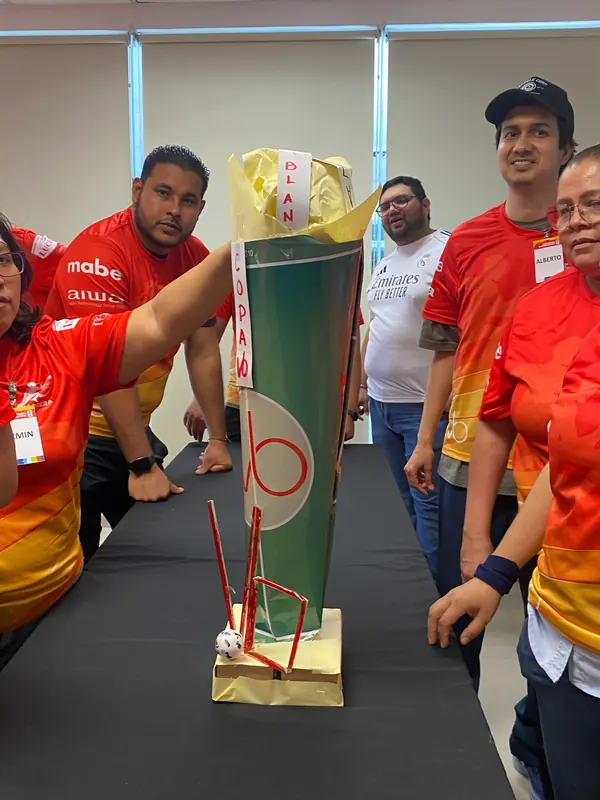 Equipo con playeras naranjas rodeando una torre verde con base amarilla durante la presentación de resultados