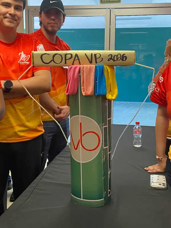 Equipo con playeras naranjas presentando una torre con el letrero «Copa VB 2026» y diademas de colores