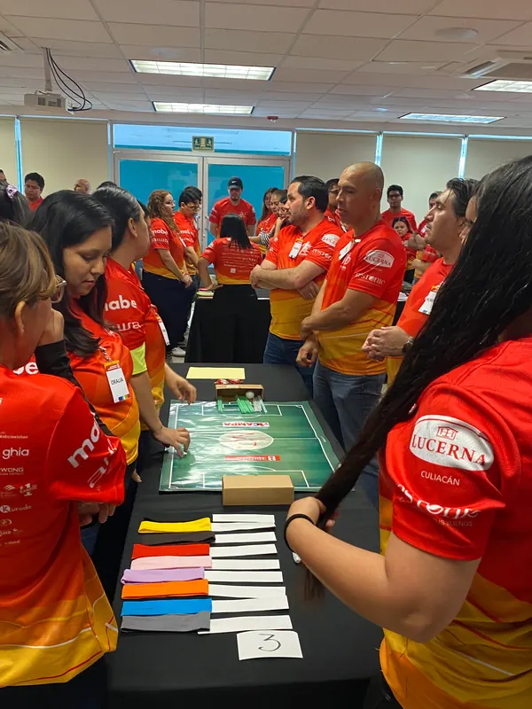 Grupo de participantes de pie alrededor de una mesa con tarjetas y diademas, trabajando en equipo