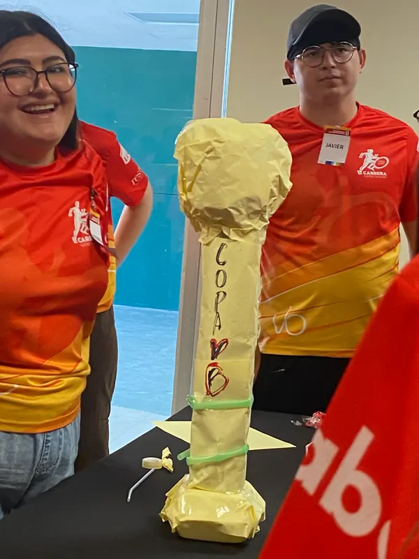 Dos participantes sonriendo junto a una torre de papel amarillo que su equipo construyó